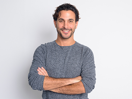 A man with curly hair stands confidently against a plain background, smiling slightly at the camera.