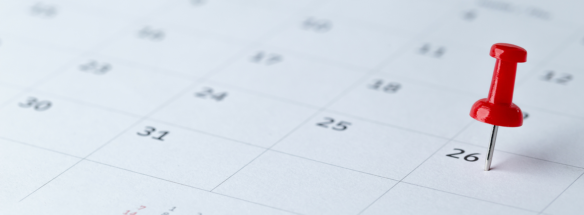The image shows a paper calendar with a red push pin pointing at a specific date, which appears to be April 26th, against a plain background.