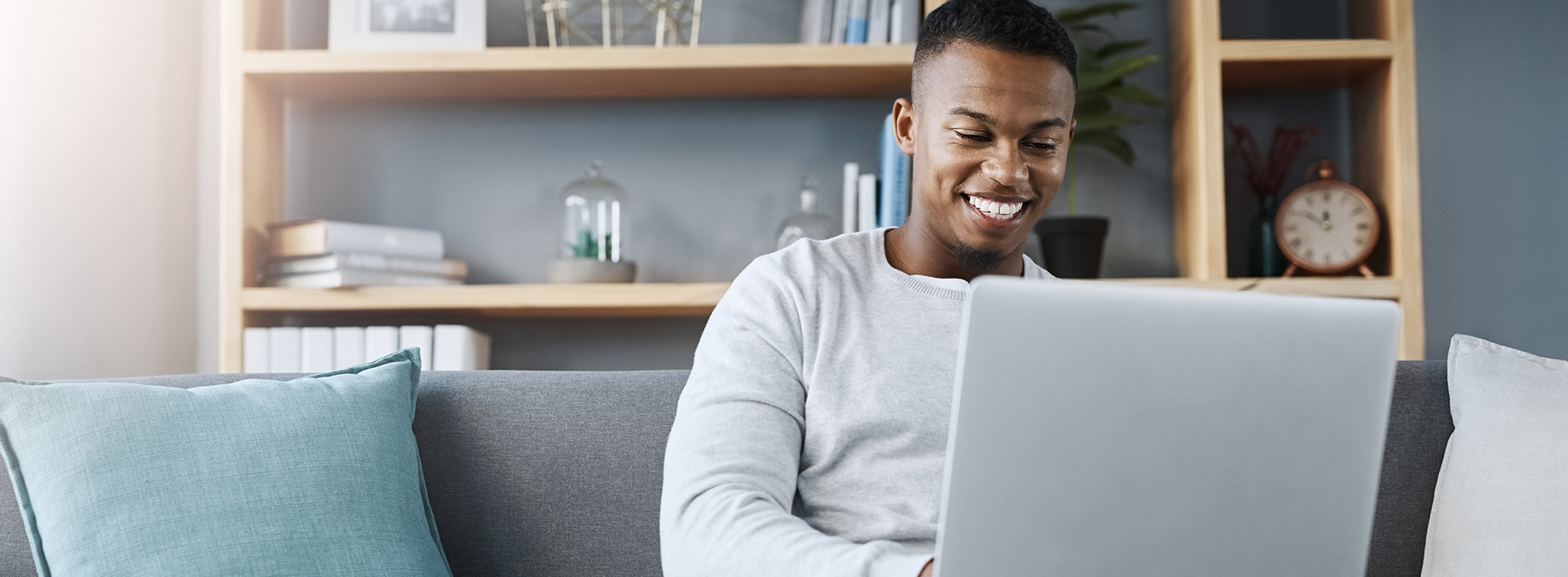 A person sitting on a couch with a laptop, smiling at the camera.