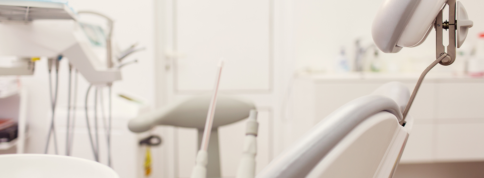 The image shows a dental office interior with various dental equipment, including chairs, a desk, and a dental chair with a lamp, set against a wall with a window.