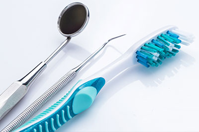The image displays a collection of dental tools including toothbrushes with blue bristles, a metal dental instrument, a pair of scissors, and a spoon-like tool on a white background.