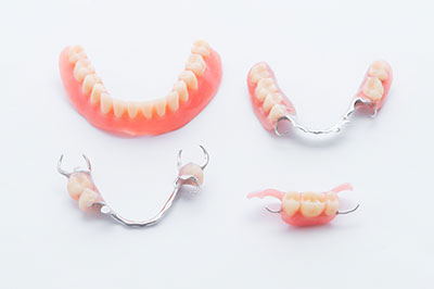 The image shows a collection of dentures with visible teeth, including some with red gums, displayed on a white background.