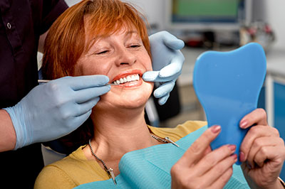 A woman seated in a dental chair with a blue dental impression device on her mouth, being attended by dental professionals who are holding her jaw open and smiling at the camera.