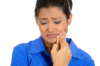 A woman with her eyes closed, holding her jaw, appears to be in pain or discomfort.