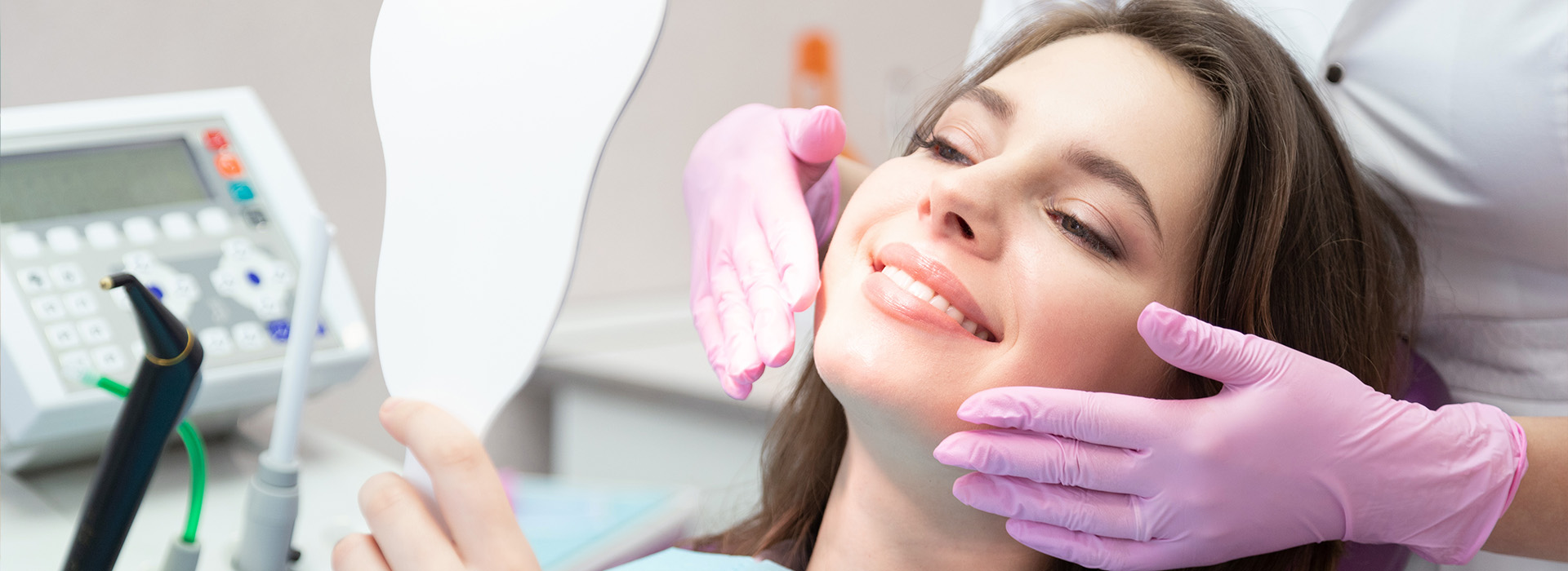The image shows a woman sitting in a dental chair with a dentist examining her teeth while wearing protective gloves and a surgical mask.