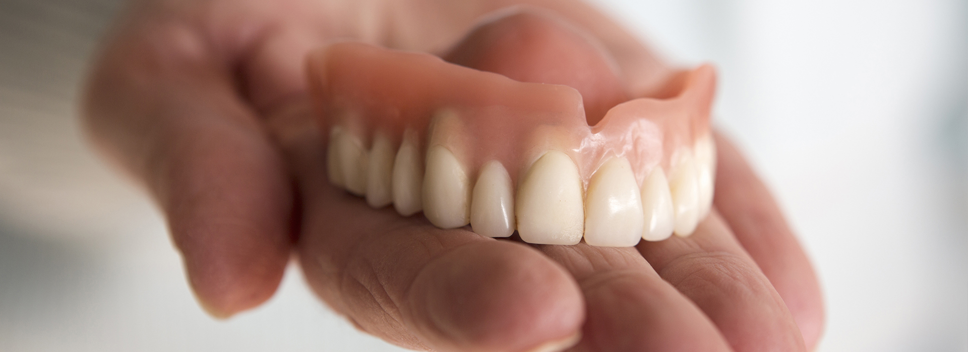 The image shows a person holding a set of dentures with an open mouth, displaying the artificial teeth within.