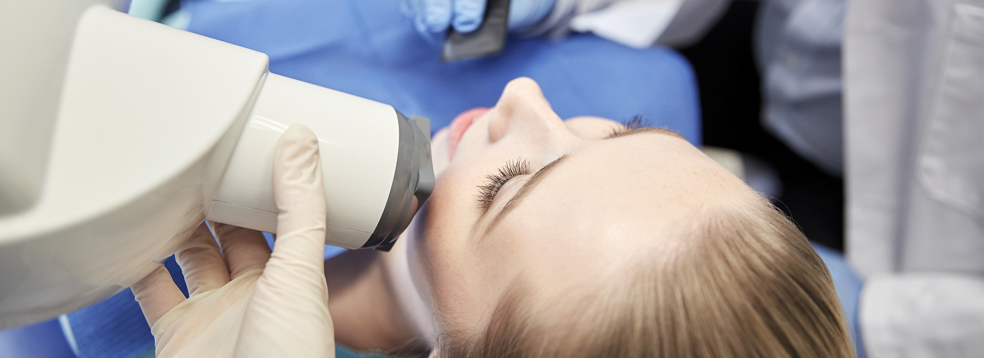 The image shows a person receiving a dental treatment with a dental mirror held up by a dental professional, focusing on the upper teeth area during the process.