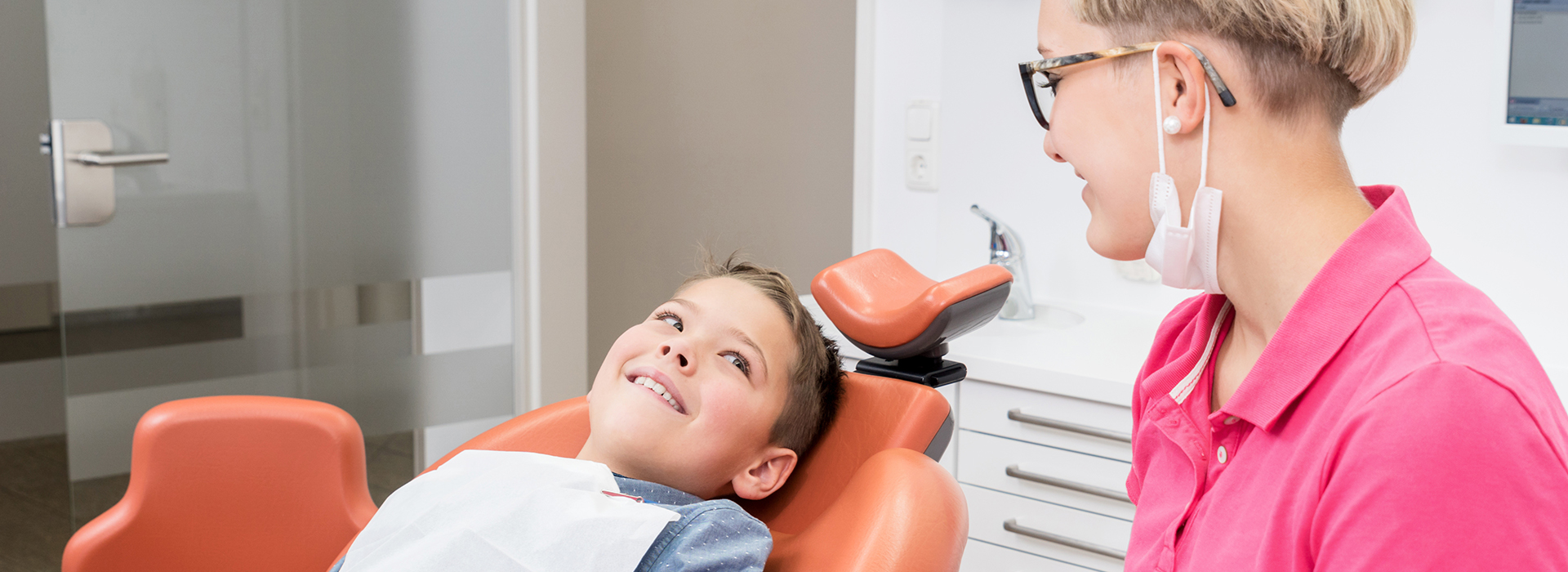 The image shows three individuals in a dental setting  two adults and a child, with one adult likely being a dentist and the other possibly a patient or a staff member.
