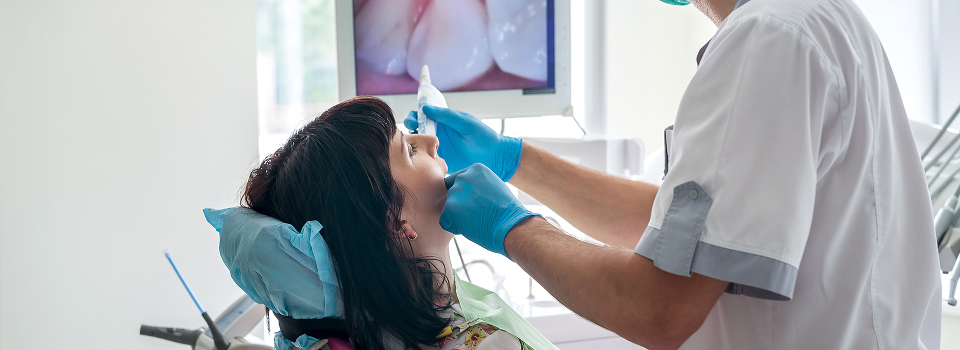 The image shows a dental professional performing a procedure on a seated patient, with the professional wearing protective gloves and a surgical mask.