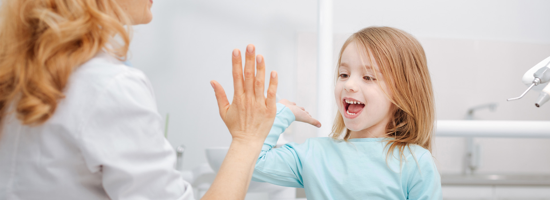 The image shows a young girl with blonde hair standing next to an adult female who appears to be interacting with her, possibly in a bathroom setting, with both individuals smiling at each other.