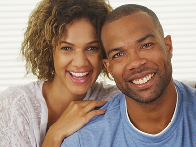 A man and woman standing close together, smiling at the camera.
