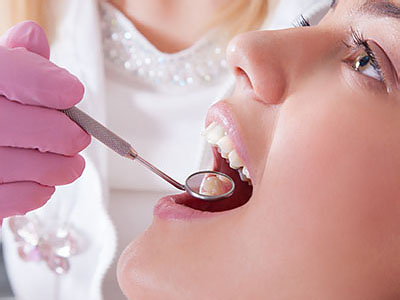 The image shows a person receiving dental care with a dentist performing a procedure using a drill, while wearing gloves and protective eyewear.