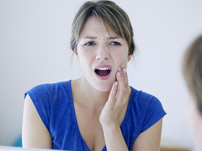 The image shows a woman with her mouth open, expressing surprise or shock, in front of a mirror while looking at her own reflection.