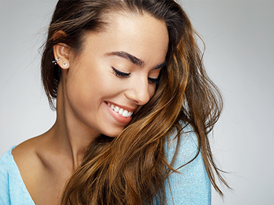 A woman with long hair smiles at the camera while posing against a light background.