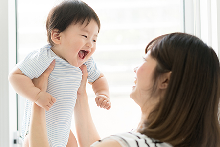An Asian woman holding a baby with an open mouth, both indoors.
