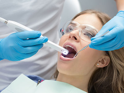 A woman receiving dental care with a device held by a professional, likely in a dental office setting.