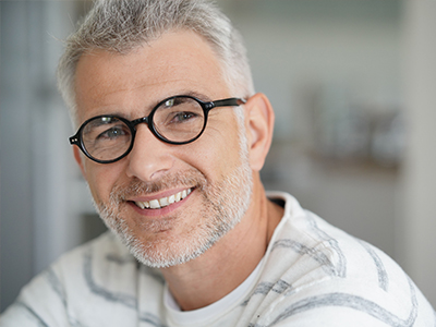 A man with glasses and a beard, smiling at the camera, wearing a white shirt with a gray stripe pattern.